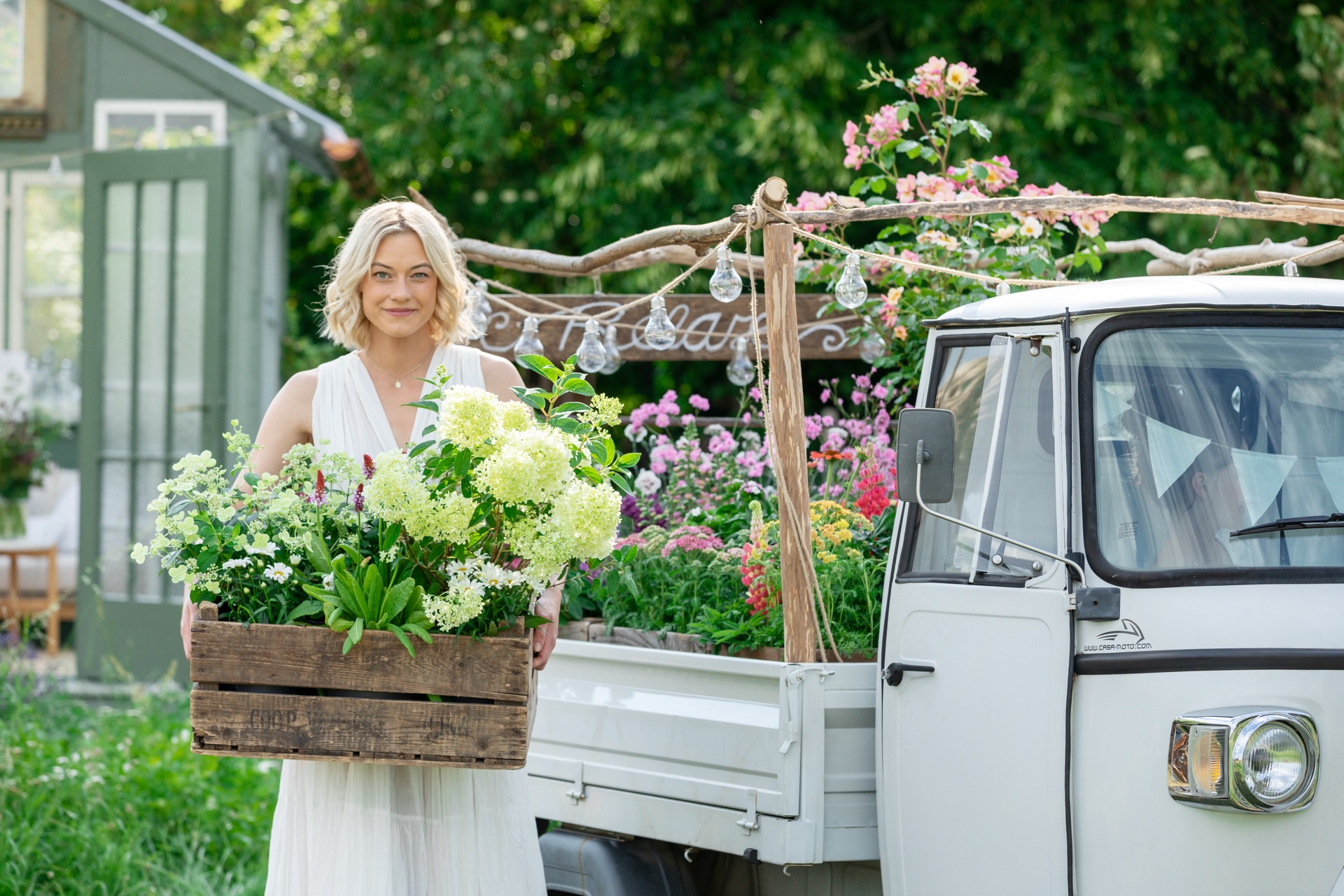 Frau mit Blumenkiste neben einem Vintage-Blumenwagen
